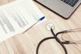 Desk with stethoscope, laptop, and form with pen