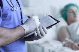 Nurse wearing gloves taking notes near patient in bed
