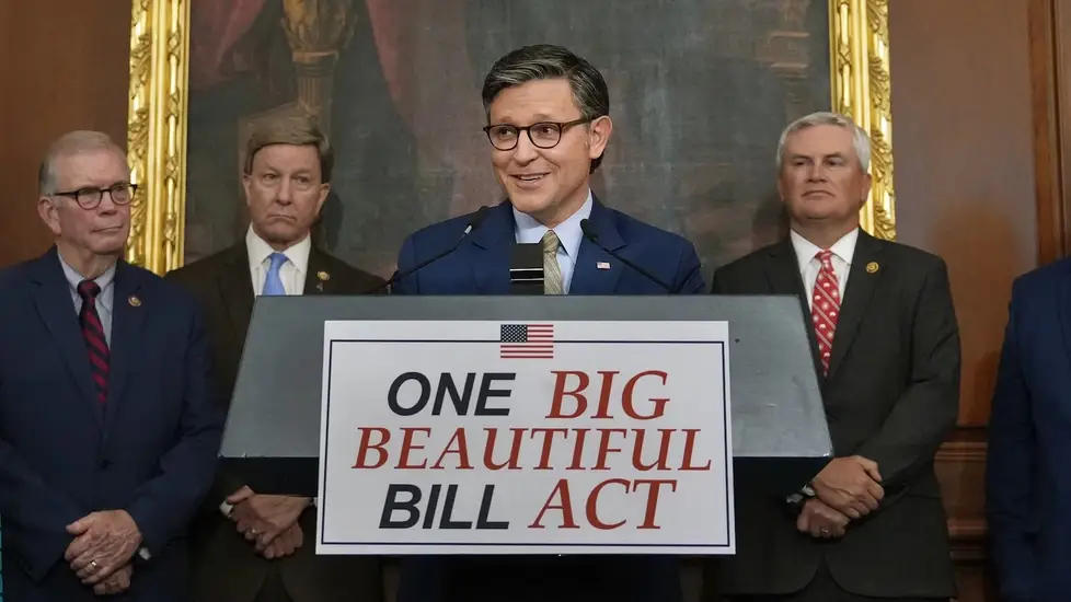 A group of lawmakers stands behind a podium displaying a sign that reads "ONE BIG BEAUTIFUL BILL ACT" with an American flag graphic at the top.