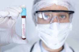 Man in ppe holding up vial of blood with covid 19 label