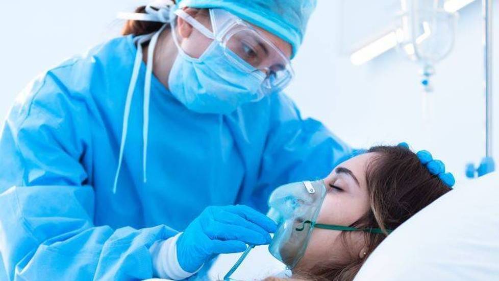Nurse wearing PPE helping patient with oxygen mask in hospital room