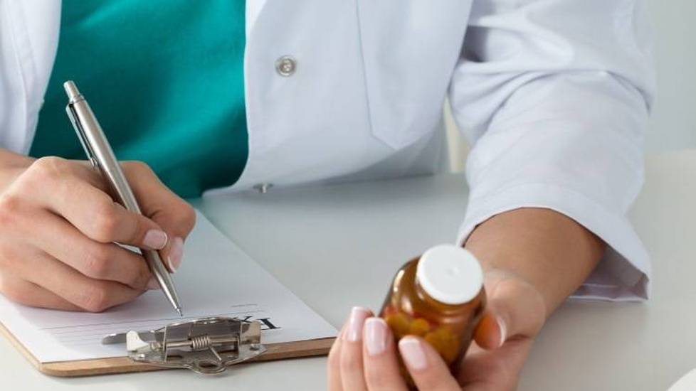 Doctor checking prescription bottle while writing note