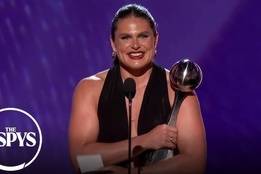 Illona Maher in a sleeveless black dress stands on stage at the ESPYS, holding a trophy and speaking into a microphone, with the ESPYS logo visible in the corner.