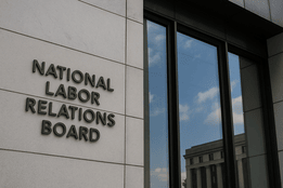 Exterior of the National Labor Relations Board headquarters building, showing the agency’s name mounted on a modern stone facade beside large reflective windows.