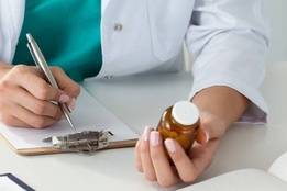 Doctor checking prescription bottle while writing note