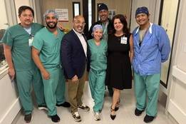 David Zambrana (navy blazer) with smiling nurses and clinicians in green scrubs in Jackson Memorial hallway.
