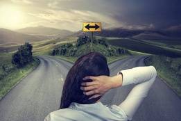 Woman at crossroads holding back of head thinking