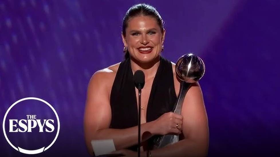 Illona Maher in a sleeveless black dress stands on stage at the ESPYS, holding a trophy and speaking into a microphone, with the ESPYS logo visible in the corner.
