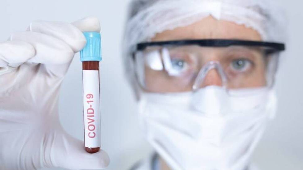 Man in ppe holding up vial of blood with covid 19 label