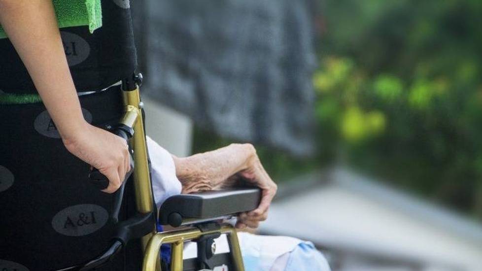 Woman helping elderly person by pushing wheelchair