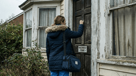 A home health nurse seen from behind knocks on the weathered door of a dilapidated house marked with a "PRIVATE PROPERTY - BEWARE" sign.