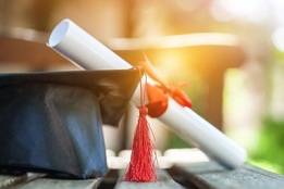 Graduation cap with rolled up diploma outside on table