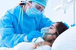 Nurse wearing PPE helping patient with oxygen mask in hospital room