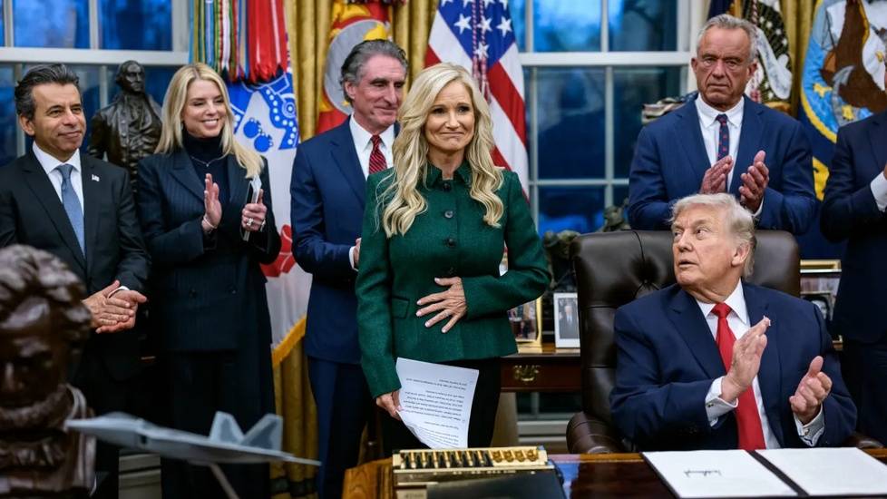 White House signing ceremony as senior administration officials applaud behind the president at the Oval Office desk.