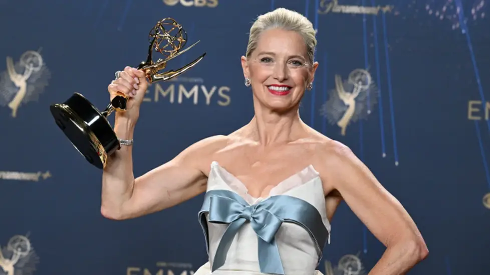 Katherine LaNasa smiles while holding her Emmy trophy at the 77th Primetime Emmy Awards, wearing a white gown with a blue bow.
