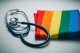 A stethoscope lies next to a neatly folded rainbow LGBTQ+ pride flag on a clean, white surface