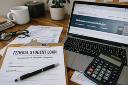 Federal student loan application form on a clipboard next to a laptop open to StudentAid.gov and a calculator.