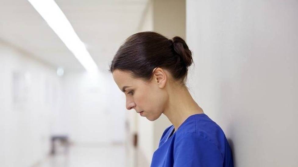 Stressed nurse leaning on wall in hospital hallway