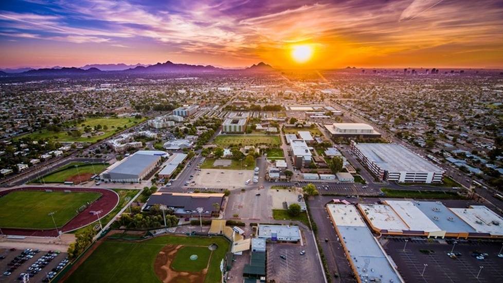 Aerial view of Grand Canyon University’s campus in Phoenix, Arizona at sunset, with athletic fields, academic buildings, and the city skyline in the distance.