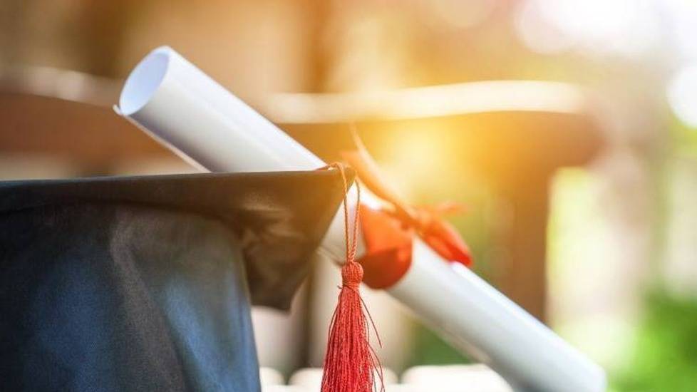 Graduation cap with rolled up diploma outside on table