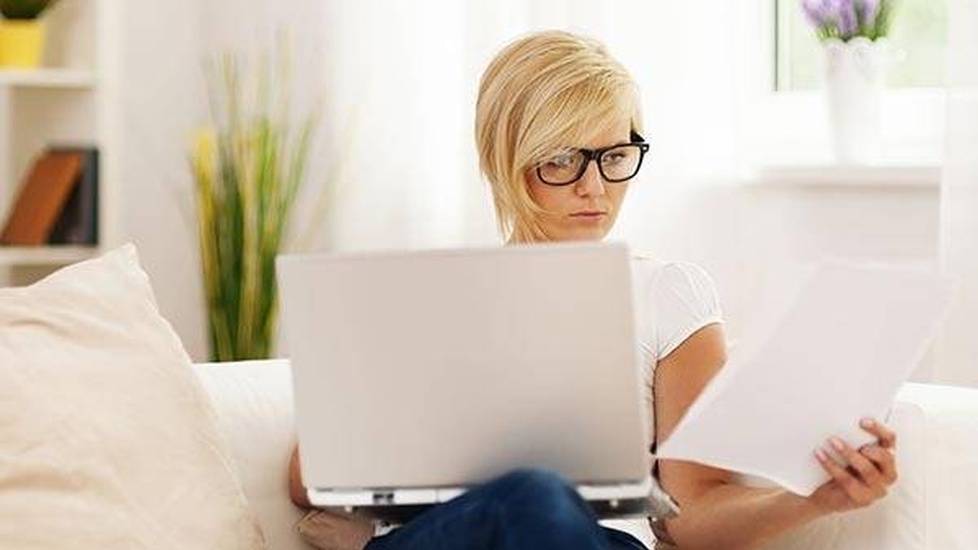 Young woman on laptop at home looking at papers
