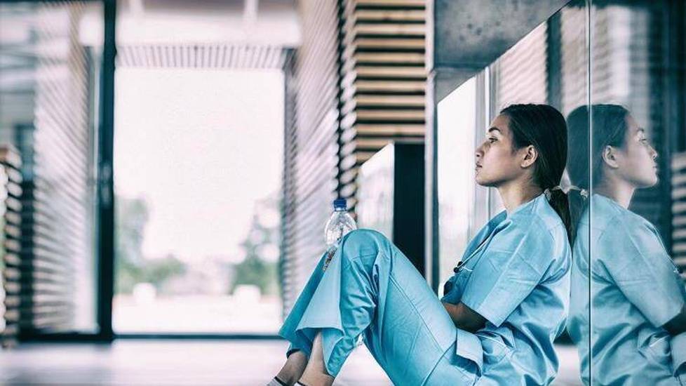 Distressed nurse sitting in empty hospital hallway