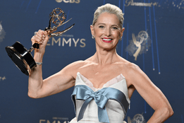 Katherine LaNasa smiles while holding her Emmy trophy at the 77th Primetime Emmy Awards, wearing a white gown with a blue bow.
