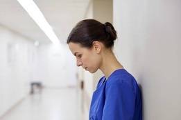 Stressed nurse leaning on wall in hospital hallway