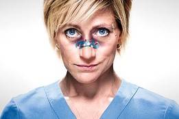Edie Falco as Nurse Jackie, in scrubs with bandages on her nose, staring intensely ahead.