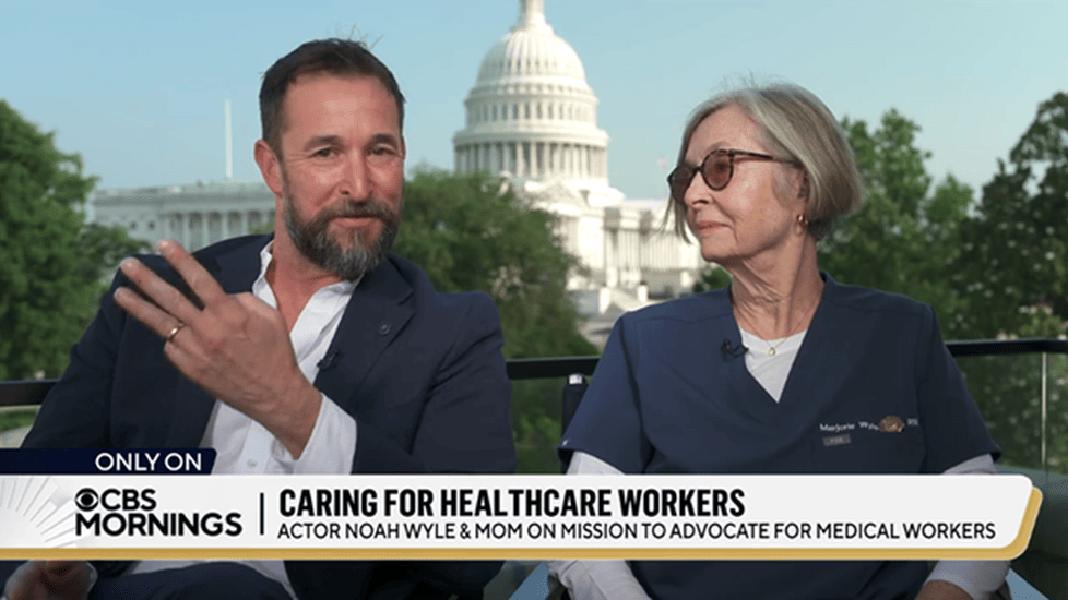Actor Noah Wyle gestures while seated next to his mother, Marjorie Wyle-Katz, a nurse, during a CBS Mornings interview with the U.S. Capitol building visible in the background.