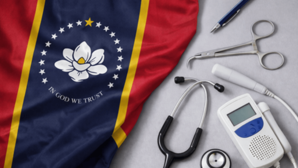 Mississippi state flag displayed beside a stethoscope and fetal Doppler, representing nurse-midwifery and maternal health care.