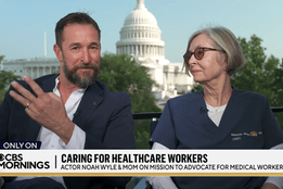 Actor Noah Wyle gestures while seated next to his mother, Marjorie Wyle-Katz, a nurse, during a CBS Mornings interview with the U.S. Capitol building visible in the background.